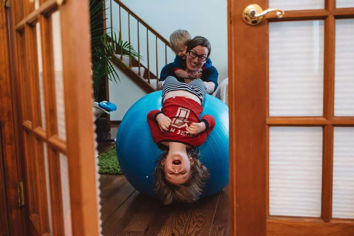 Mom playing with son on a yoga ball while her other child climbs on her back