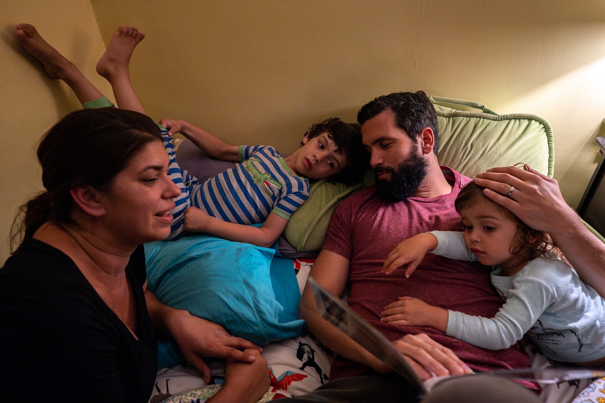 Mom and dad trying to read a book to their two boys in bed.