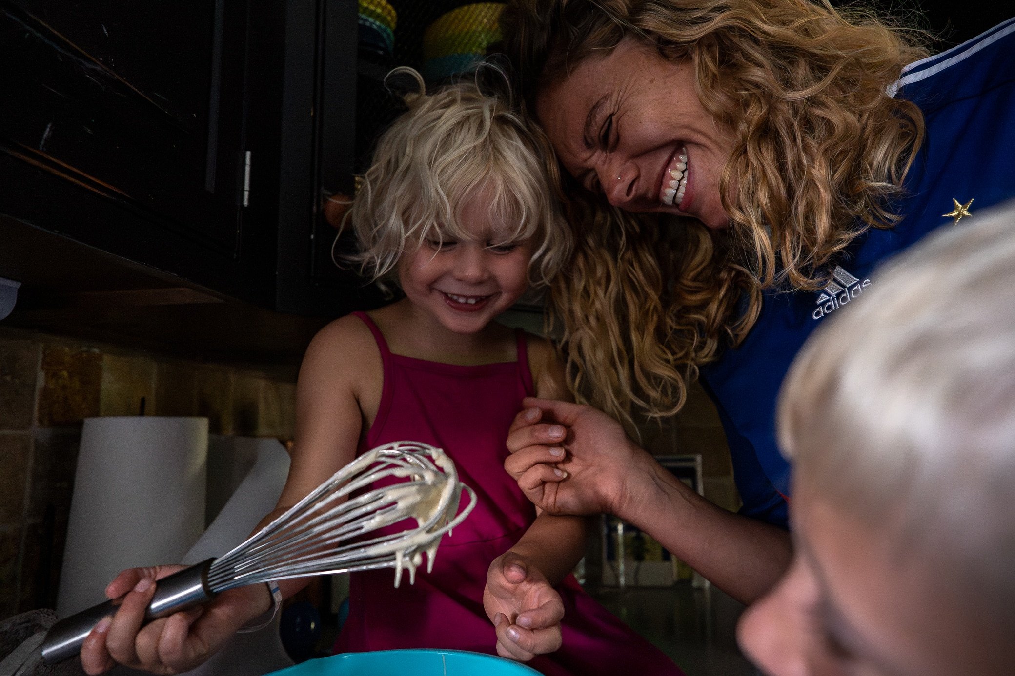 Mom laughing with daughter while daughter is holding a whisk covered in pancake batter