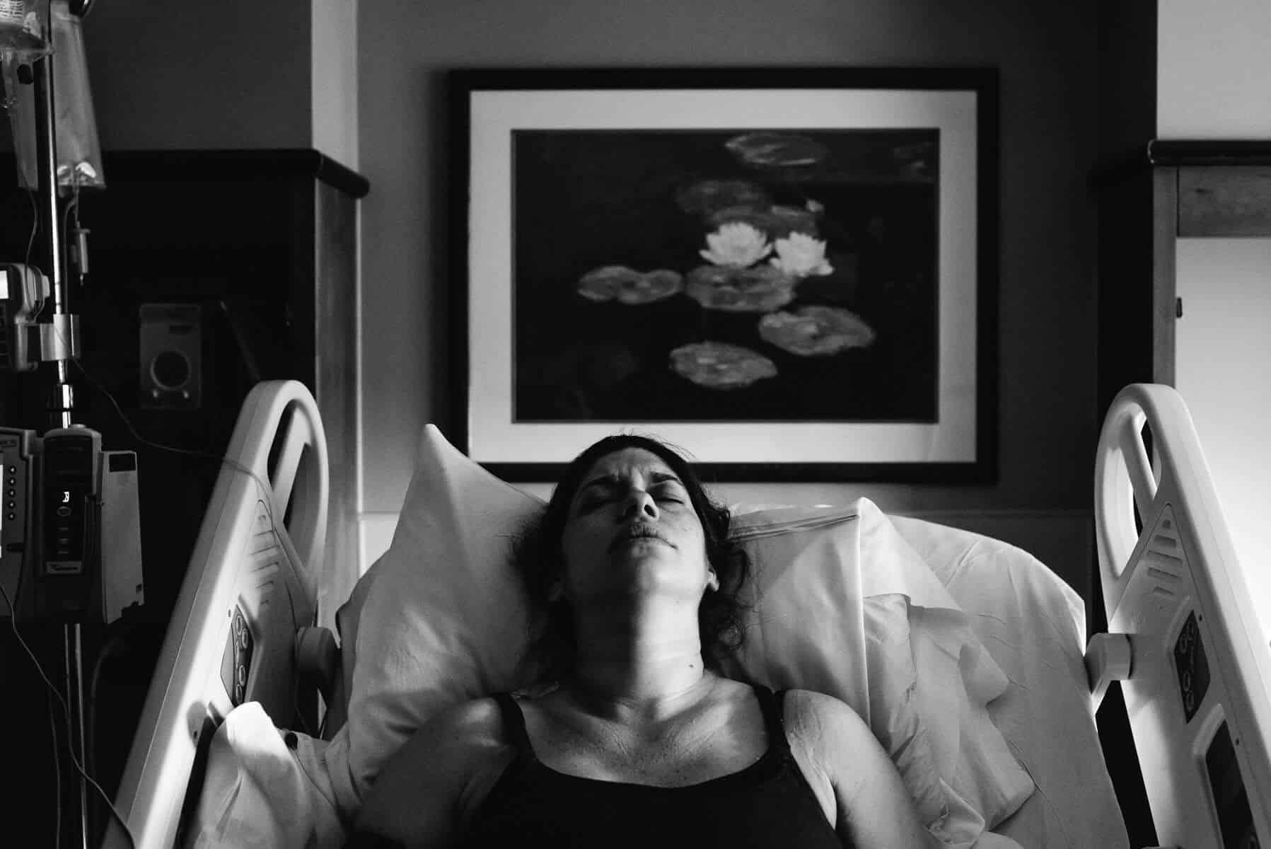 Black and white style birth photo of mother laboring in hospital, eyes closed and head tilted up.